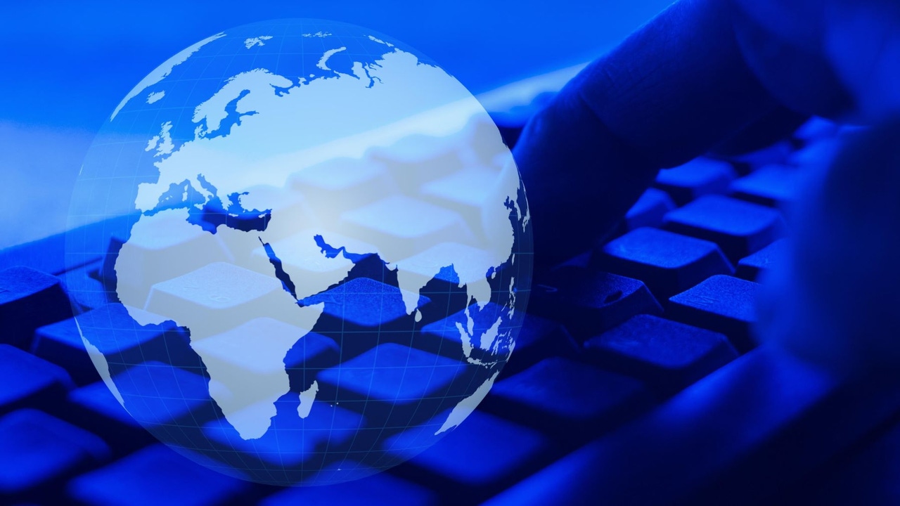 Globe superimposed over image of person typing on keyboard; blue tint Globe superimposed over image of person typing on keyboard; blue tint