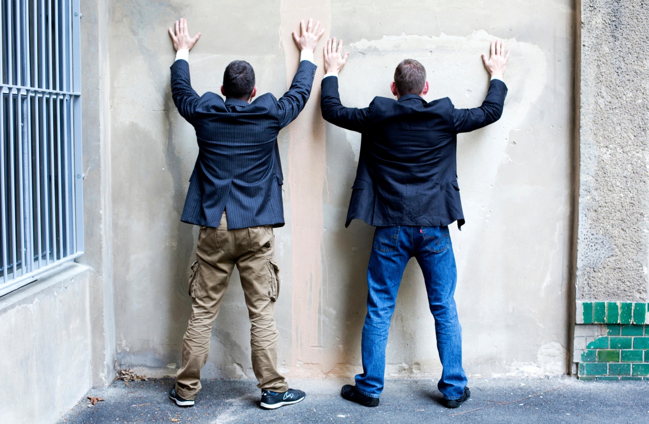 Two men with hands up facing a wall like they are being arrested Two men with hands up facing a wall like they are being arrested