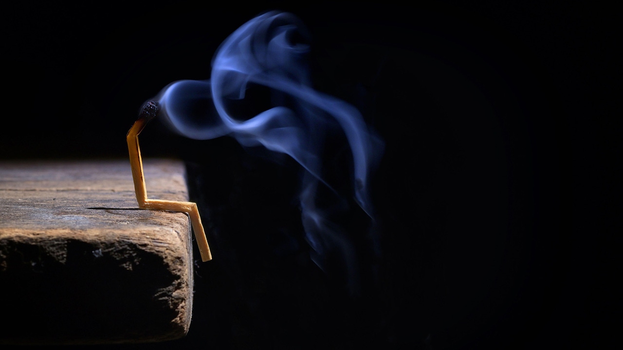 Conceptual burned out and smoking wooden match on black background, with match folded to look like a human sitting Conceptual burned out and smoking wooden match on black background, with match folded to look like a human sitting