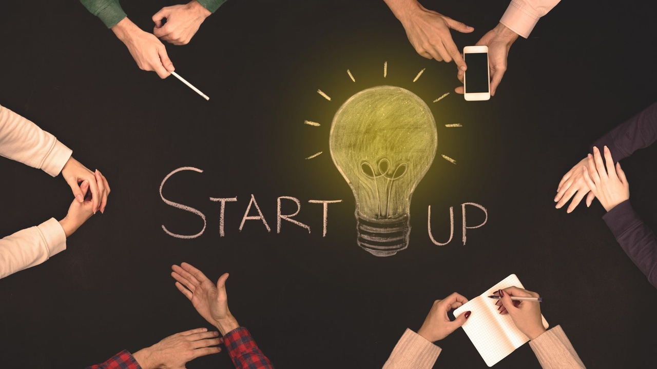 People sitting around a table--the word "Startup" is in the middle of the table, with a lit lightbulb in the middle of the word People sitting around a table--the word "Startup" is in the middle of the table, with a lit lightbulb in the middle of the word