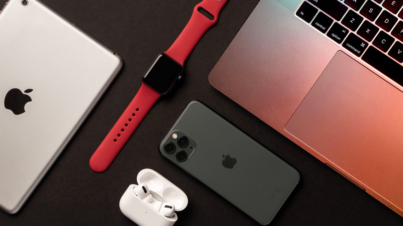An iPad, iPphone, Apple Watch, AirPods, and MacBook laid out on a black table