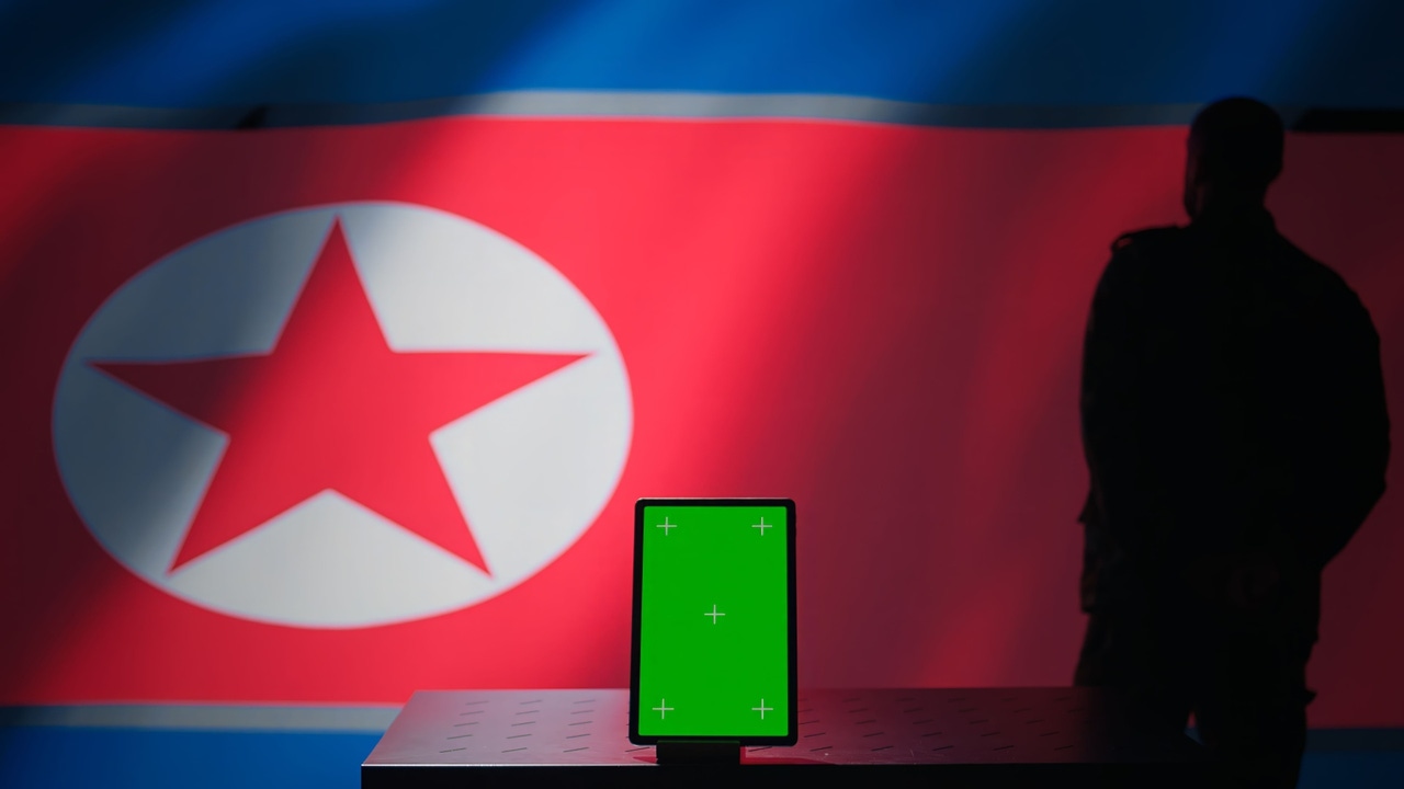 Tablet screen in front of shadowy North Korean flag and hooded figure Tablet screen in front of shadowy North Korean flag and hooded figure