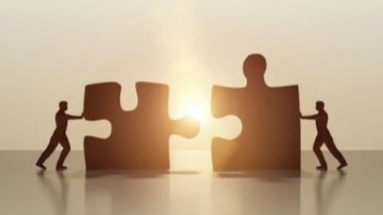 Silhouettes of two people pushing two giant puzzle pieces together