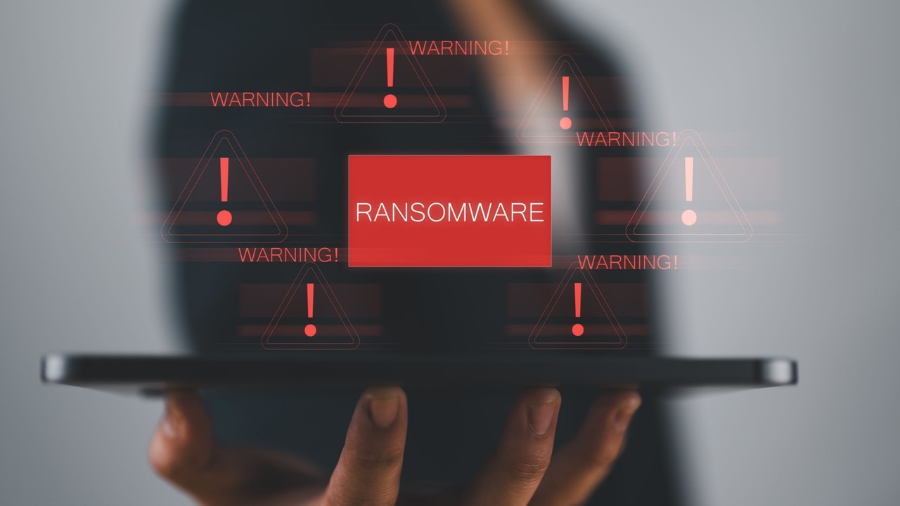 A person in the background holding a device outward, the word "Ransomware" in a bold red box in the middle with warning alerts around it A person in the background holding a device outward, the word "Ransomware" in a bold red box in the middle with warning alerts around it