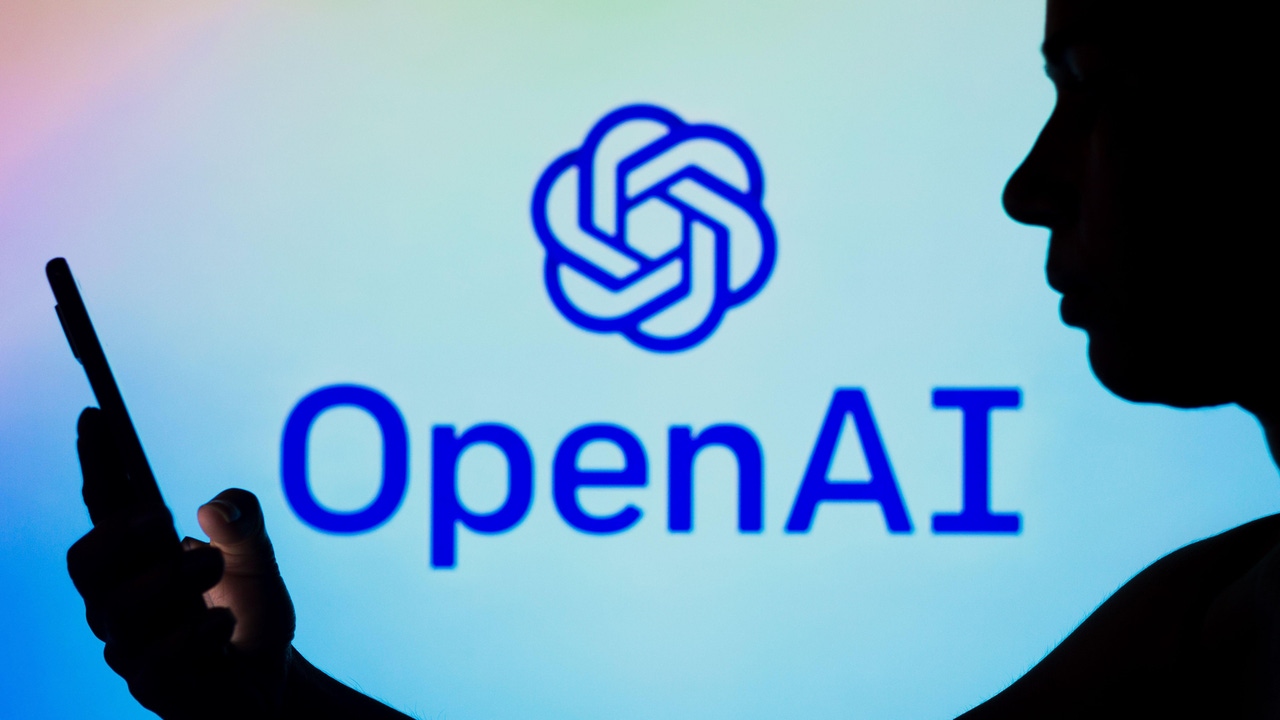 A silhouette of a man holding a smartphone, in front of a screen displaying OpenAI's logo A silhouette of a man holding a smartphone, in front of a screen displaying OpenAI's logo