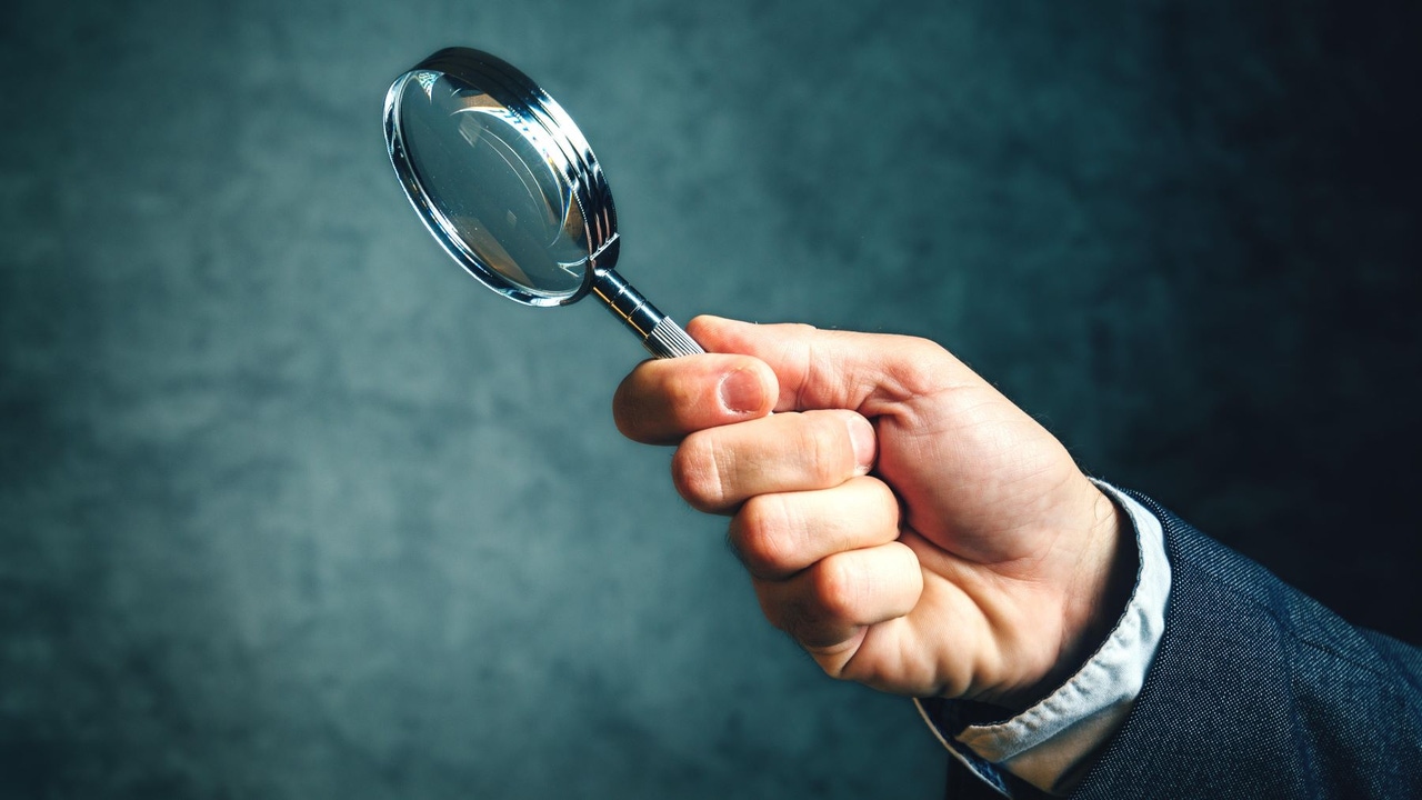 Hand holding a magnifying glass against a dark background Hand holding a magnifying glass against a dark background