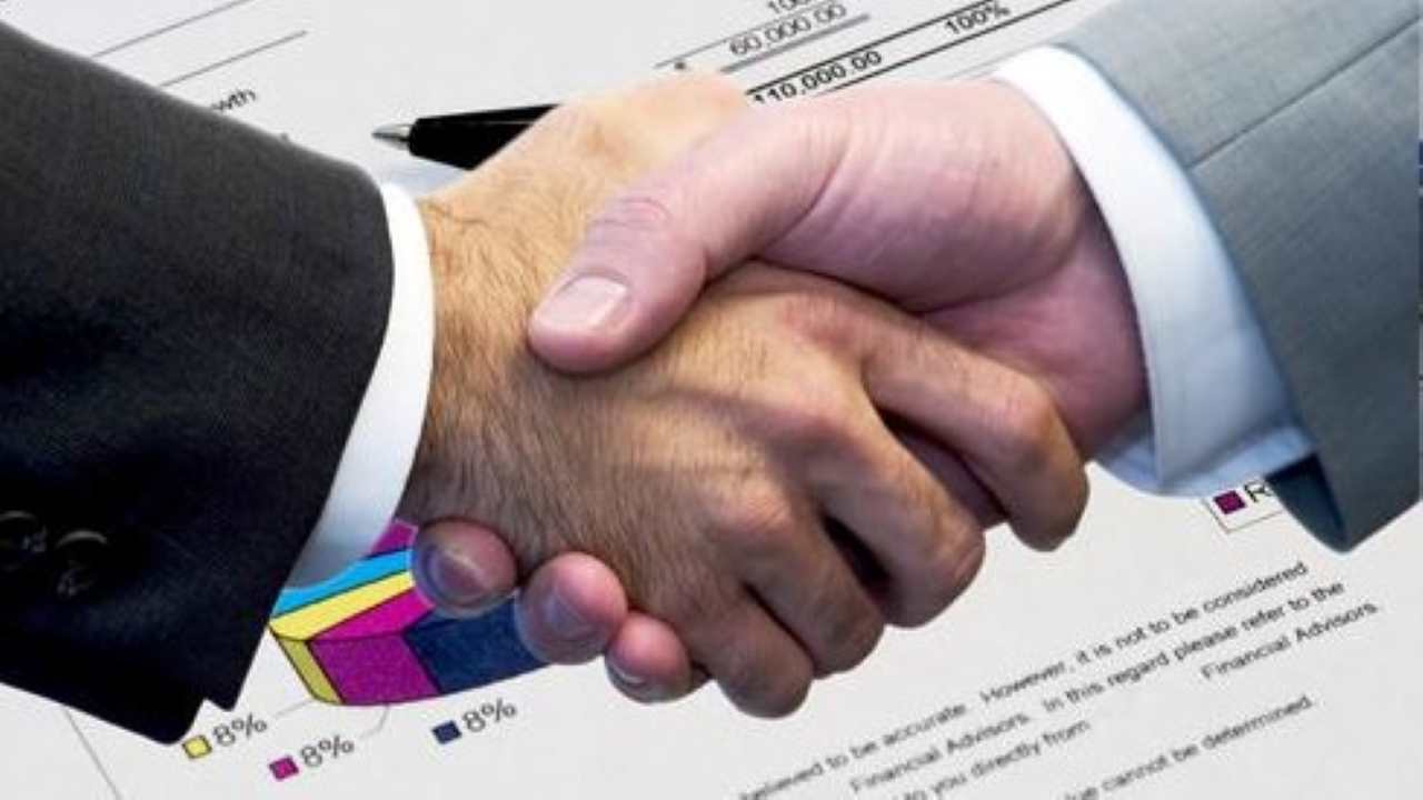 Two people, one wearing a dark suit and another in a grey suit, shaking hands against the backdrop of charts Two people, one wearing a dark suit and another in a grey suit, shaking hands against the backdrop of charts